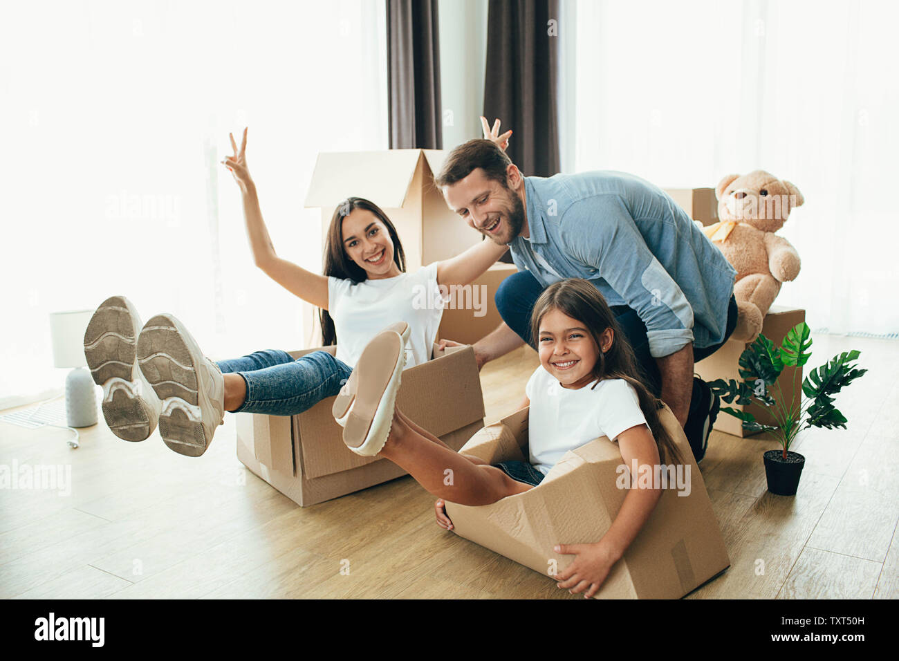 Happy father playing with his child and wife in new house. It is wonderful moving to a new apartment Stock Photo