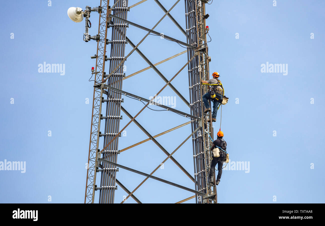 Communication maintenance. Two technicians climbing on telecom tower antenna against blue sky background Stock Photo