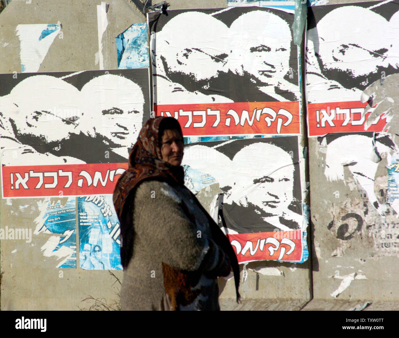 A Palestinian woman stands near a concrete barrier with anti-Sharon campaign posters of Israeli Prime Minister Ariel Sharon and his son, Omri, reading, 'Forward to Prison'  outside  Jerusalem, January 5, 2005.  Israeli Prime Minister Ariel Sharon suffered a major stroke late Wednesday night and survived more than nine hours in surgery in Hadassah Ein Kerem Hospital, in Jerusalem, where he remains in serious, but stable condition.  Dr. Shlomo Mor-Yosef said that Sharon survived intensive surgery to stop widespread bleeding in his brain, but is heavily sedated and connected to a respiratory syst Stock Photo