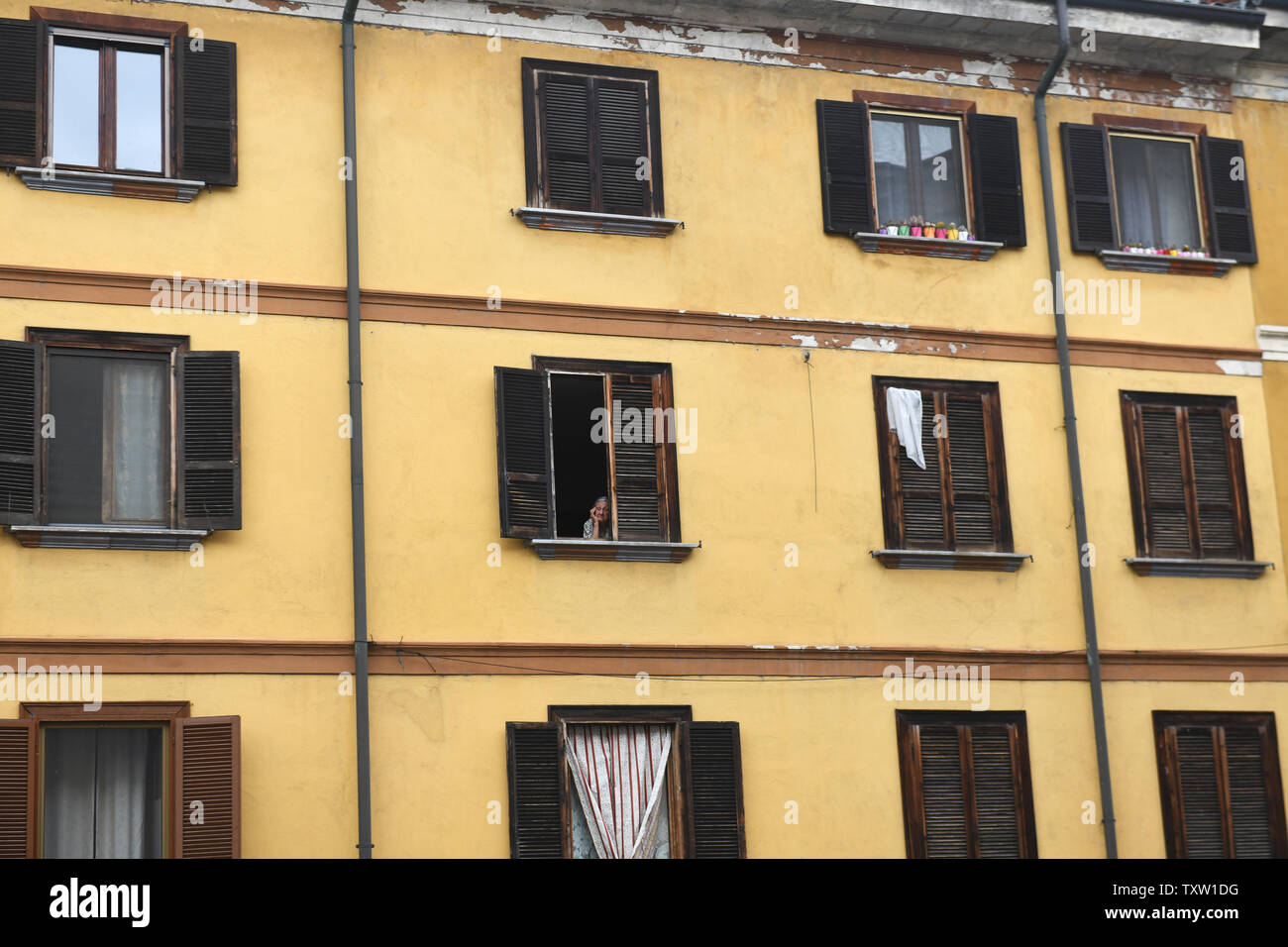 Old lady peering out of apartment window in Italy, Europe Stock Photo