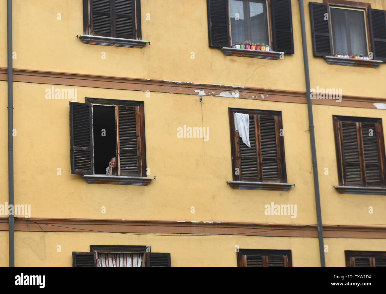 Old lady peering out of apartment window in Italy, Europe Stock Photo