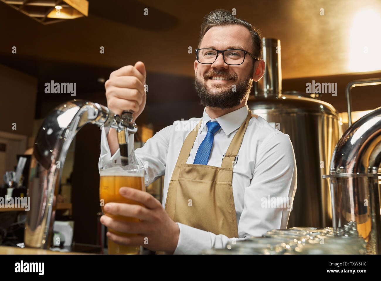 Positive bartender in glasses pouring lager beer in glass. Adult