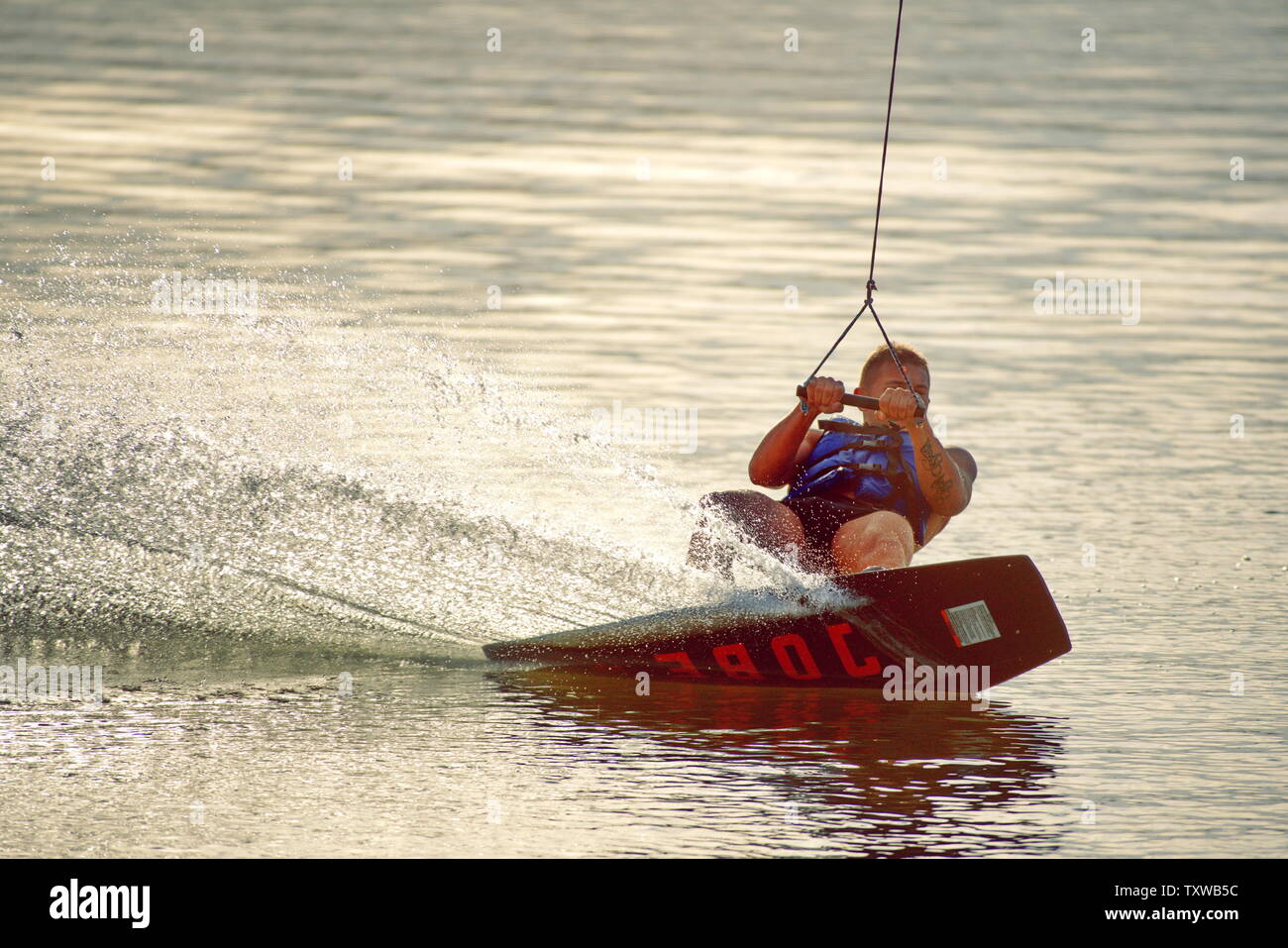 Surfer wakeboarding an jumping Ollie at golden sunset. Skilled