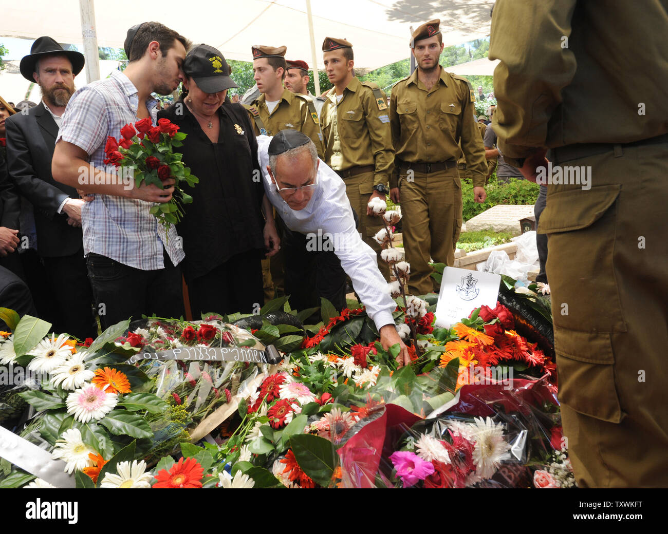 Stuart Steinberg  (R), from California, places a stone on the flower covered grave of his slain son, American-Israeli soldier Max Steinberg, 24, after his funeral in the military cemetery on Mt. Herzl in Jerusalem, Israel, July 23, 2014.  Steinberg, a native of Los Angeles, California, immigrated to Israel and enlisted in the Israel Defense Forces in 2012, where he served as a sharpshooter in the elite Golani Brigade. He was among the 13 soldiers killed by Palestinian militants in the Gaza Strip on Sunday. Twenty-nine Israeli troops have been killed since the army launched a ground incursion i Stock Photo