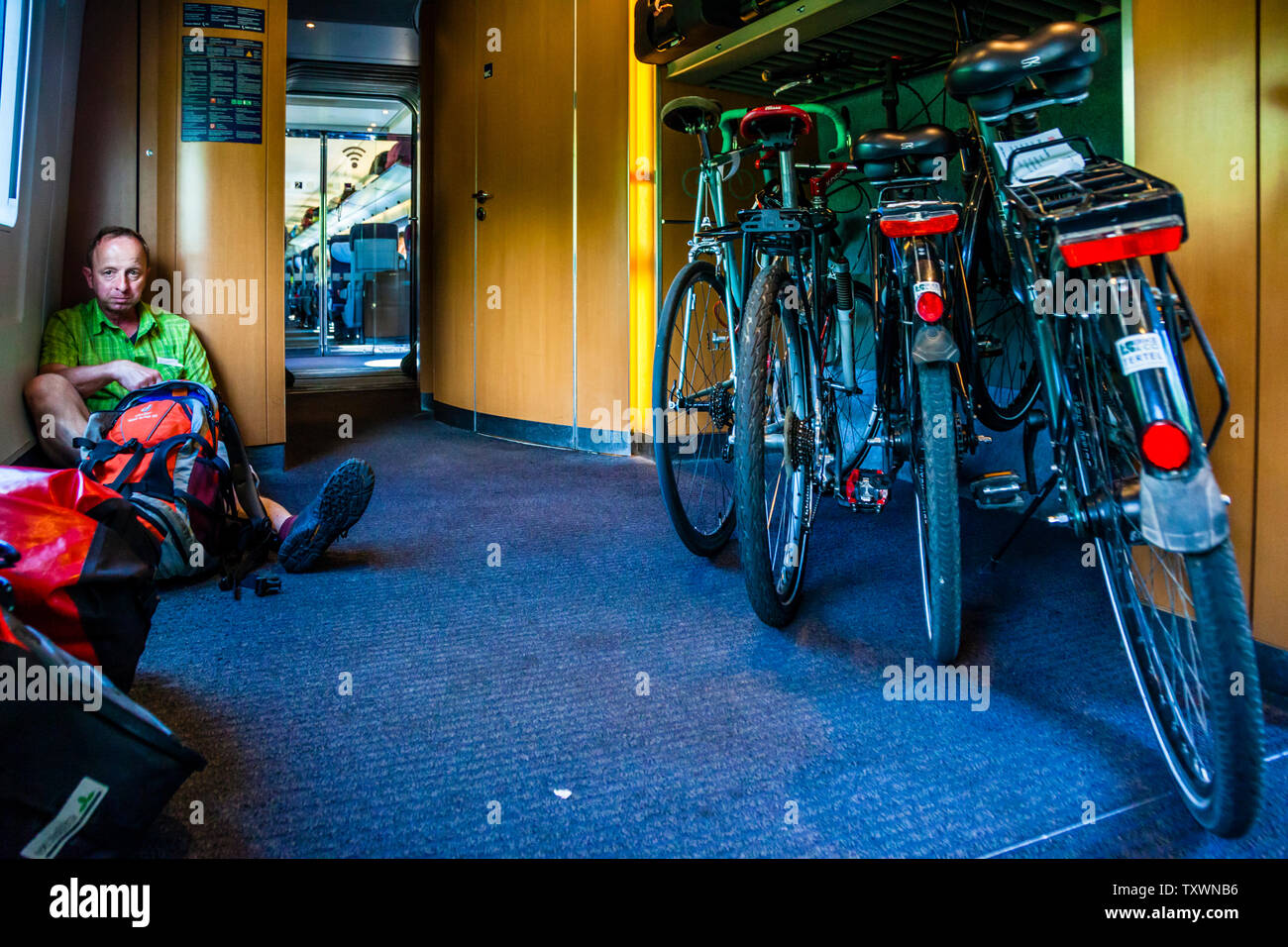A cycling traveller, possibly Georg Berg himself, sits on the floor of the vestibule next to his luggage. Several bicycles are stowed in the train's bicycle compartment opposite. Stock Photo