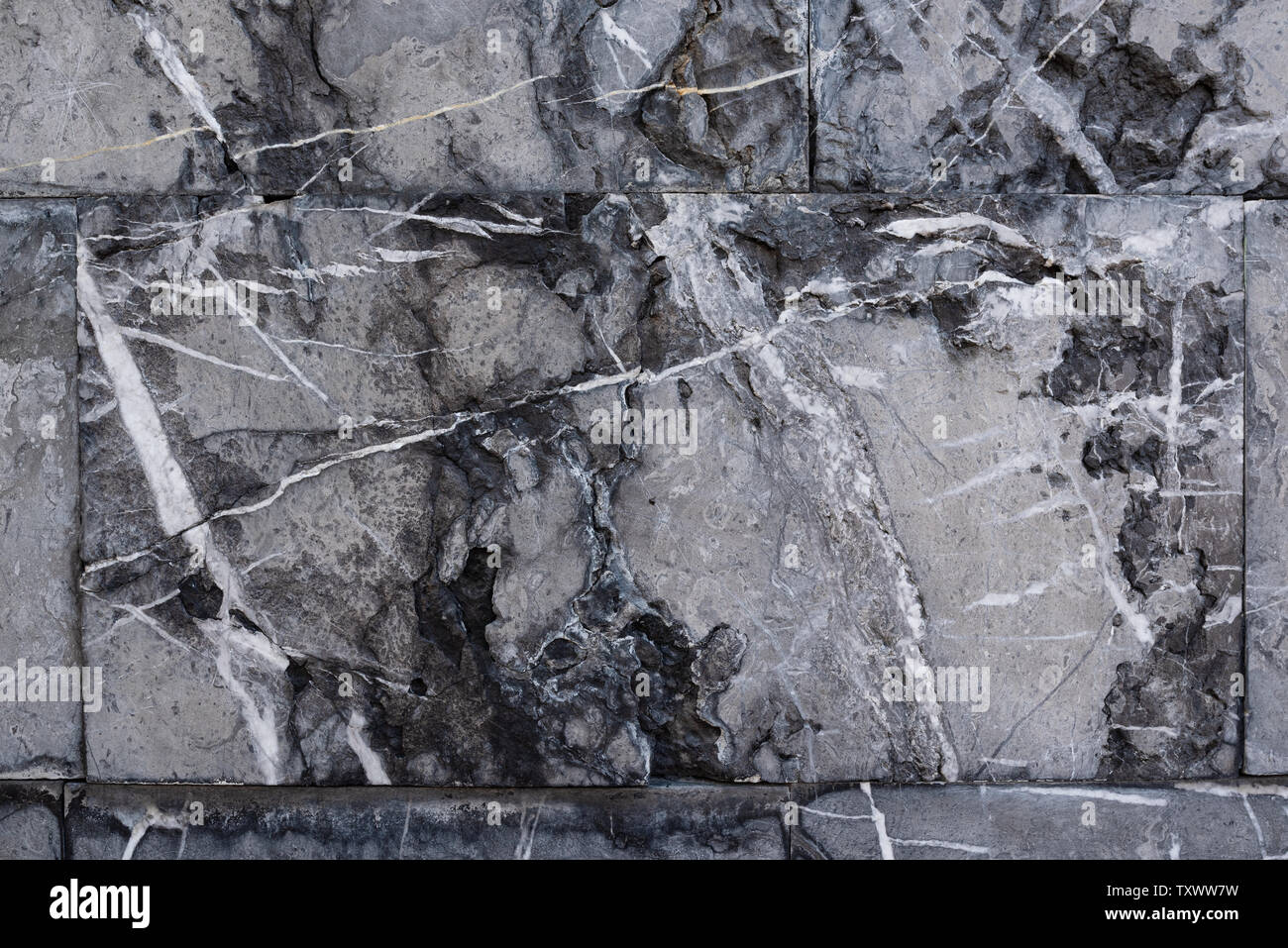 Background from gray marble blocks. A wall of rough stone with black potholes and white lines Stock Photo