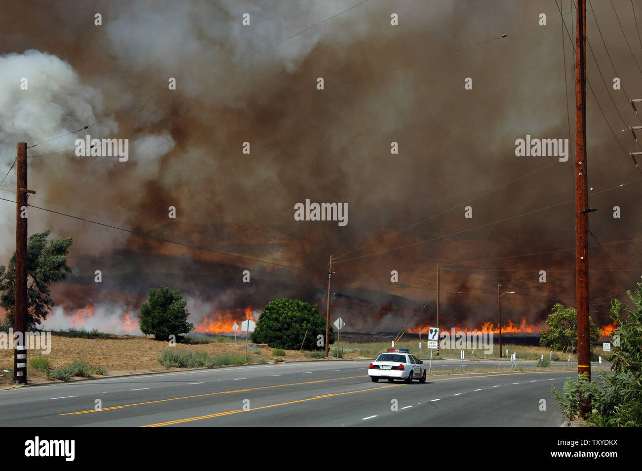 A local policeman patrols the road adjacent to a controlled burn to help combat a wildfire in Yucaipa, California on July 16, 2006. Crews battling wildfires that had destroyed 58 homes and blackened more than 110 square miles faced a threat of thunderstorms Sunday that could produce lightning capable of starting new blazes or heavy rain that would flood the newly denuded land. (UPI Photo/Jim Ruymen) Stock Photo