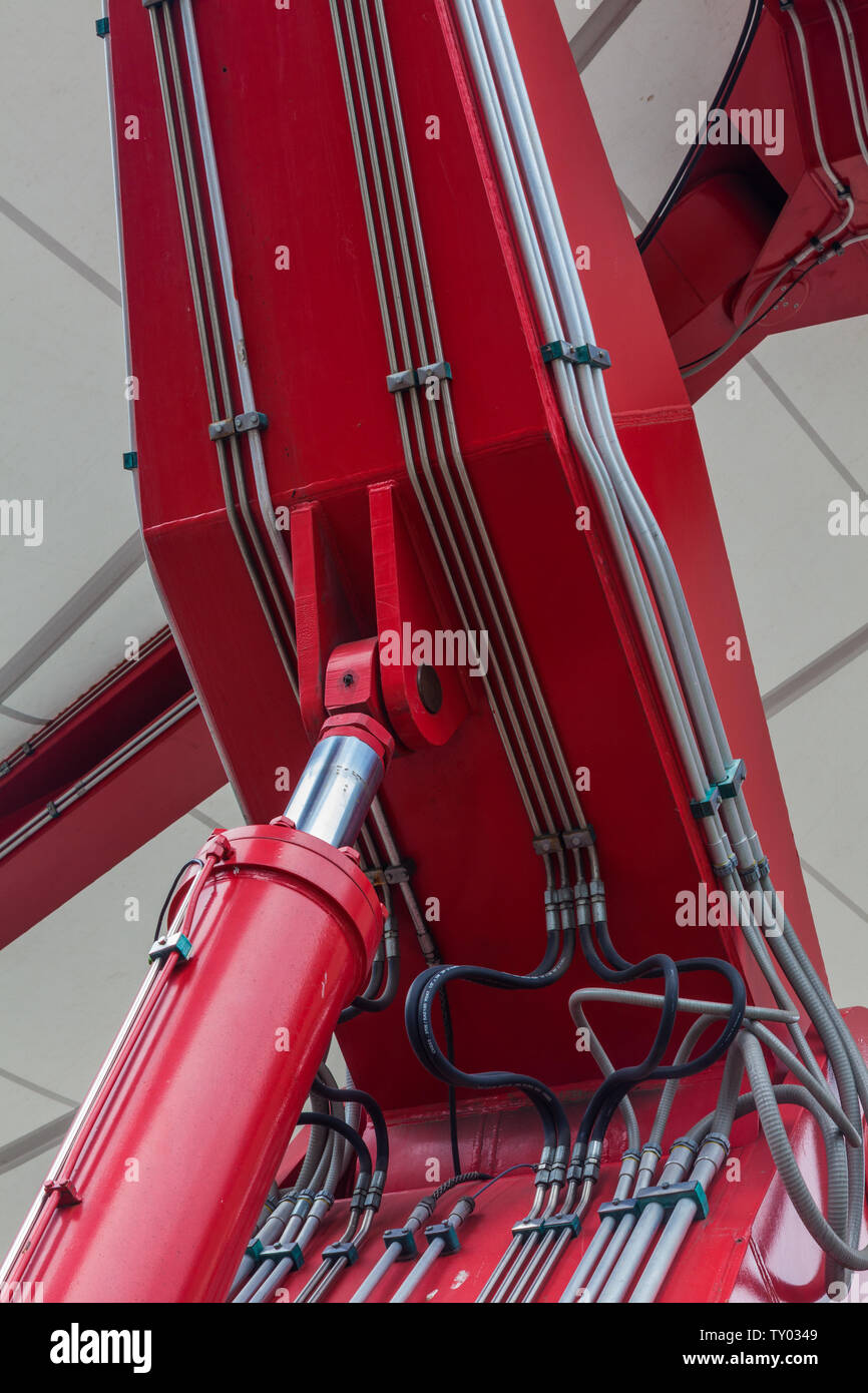 Red hydraulic cylinder with associated piping and hoses at an