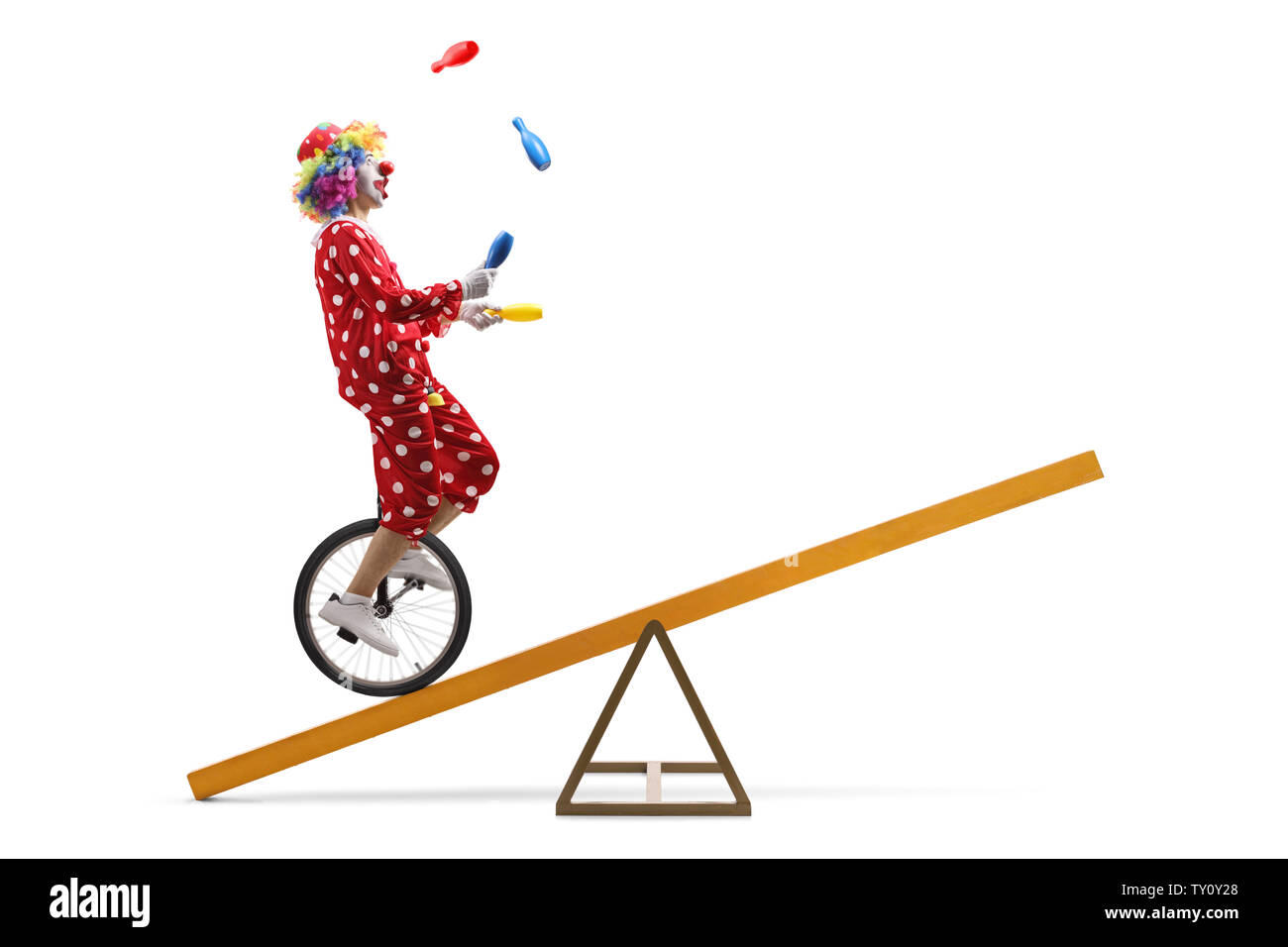 Full length shot of a clown riding a unicycle on a beam and juggling isolated on white background Stock Photo