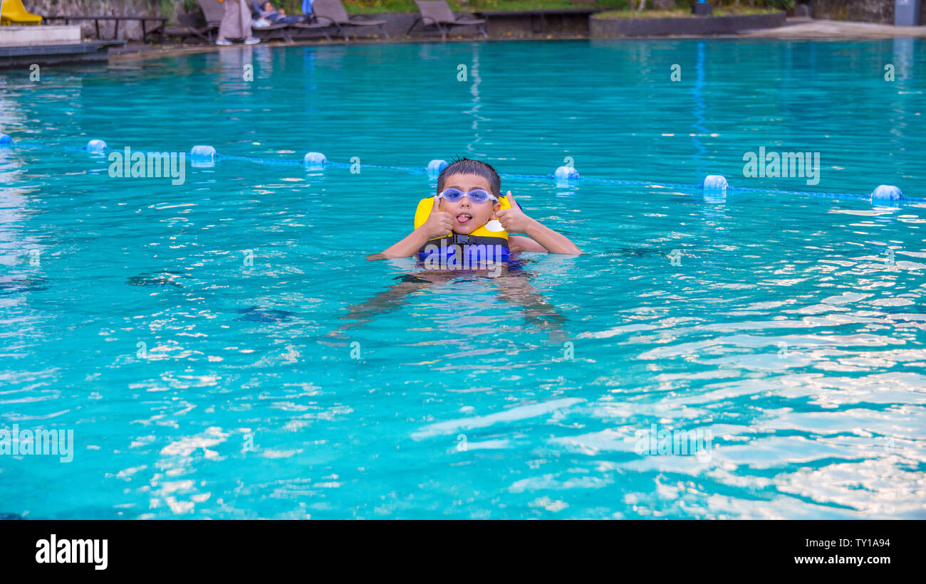 Boy swimming with life vest and googles on poking out his tongue