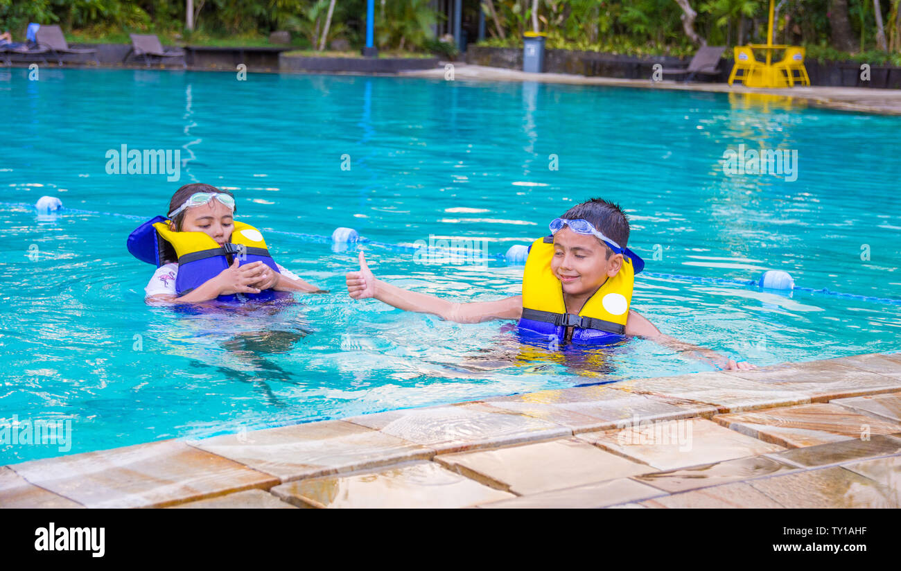 Boy swimming with life vest and googles on poking out his tongue