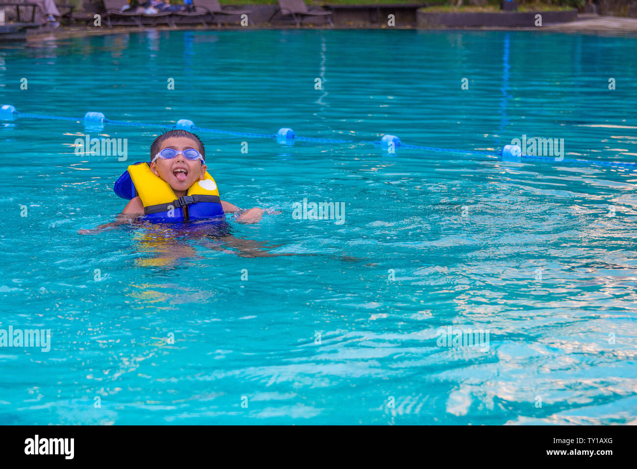 Boy swimming with life vest and googles on poking out his tongue