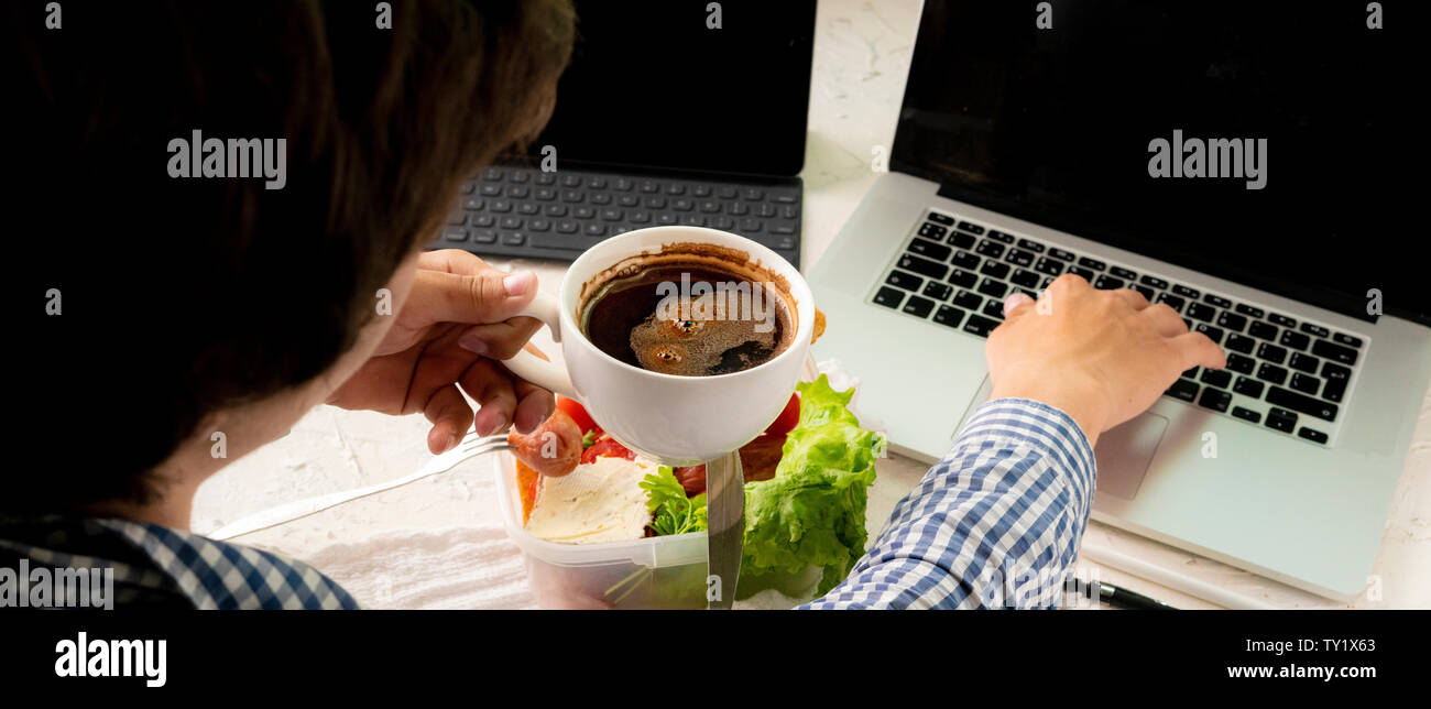 young male taking meal in front of the laptop while working, bad habit and obesity concepts Stock Photo