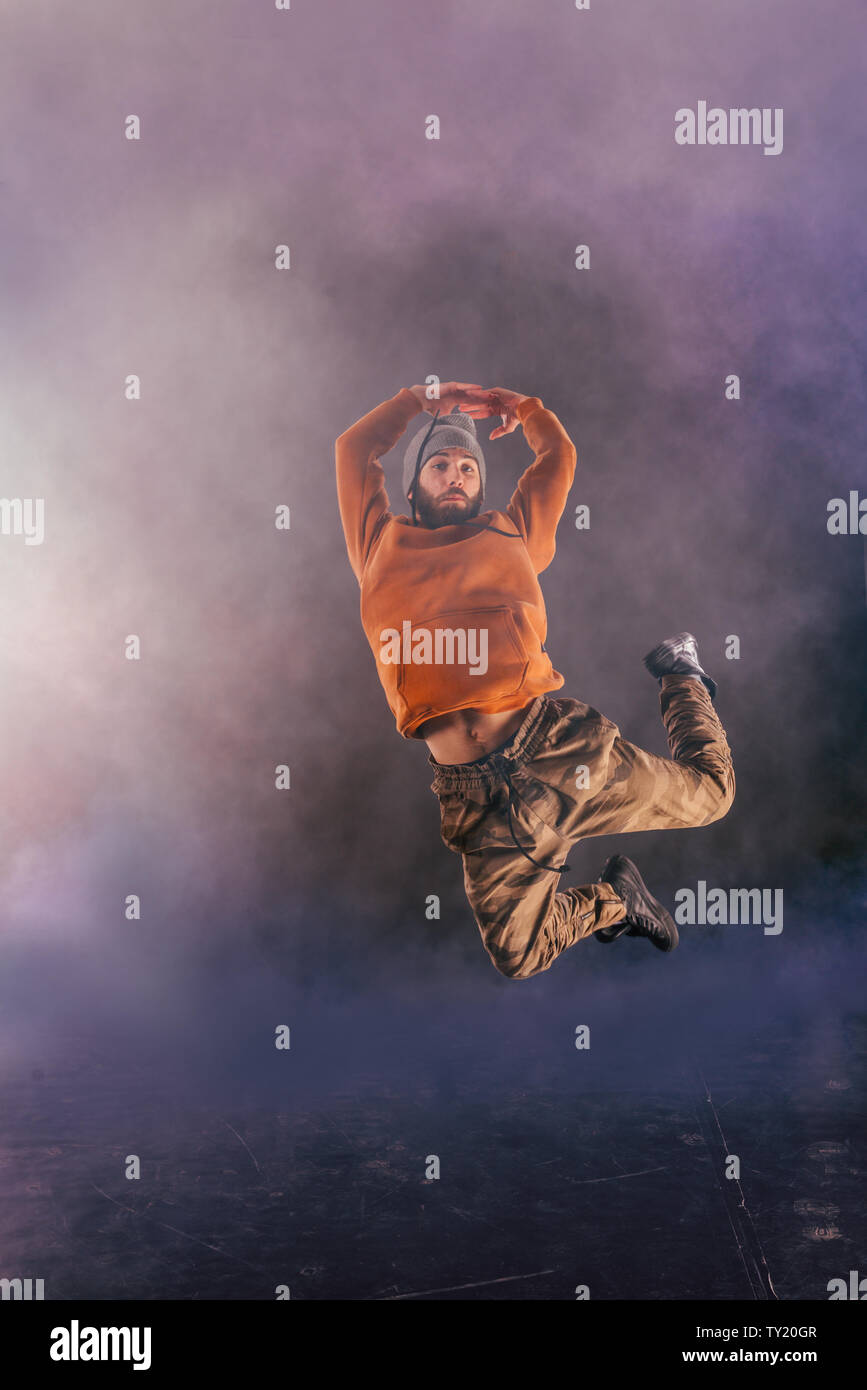 Male breakdancer jumps off high in the air while performing a cool dance move, a lot of smoke in the background. Stock Photo