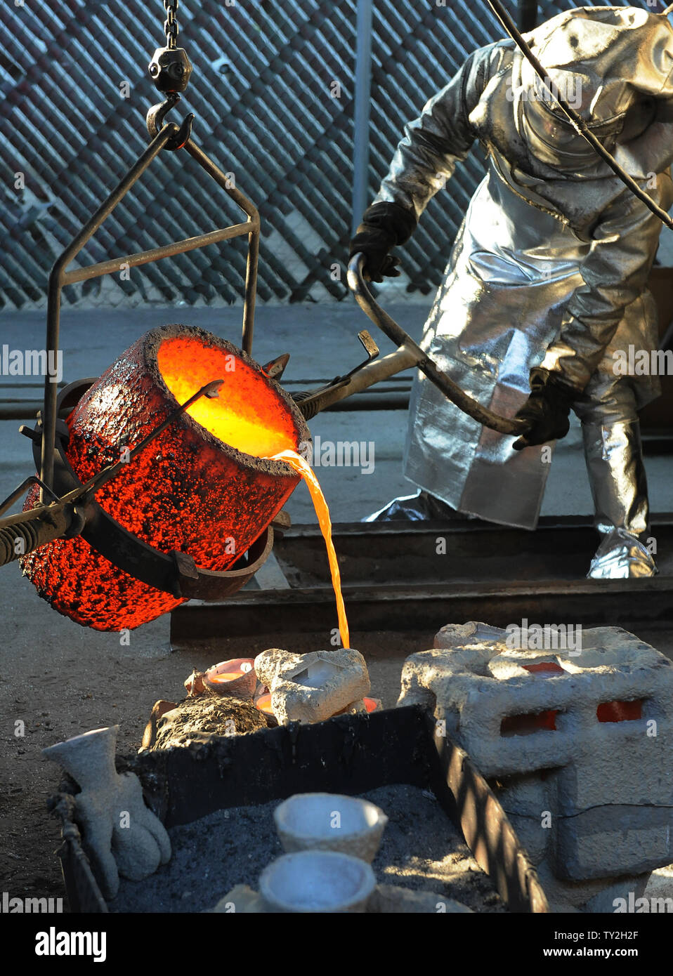 Workers in fire suits pour molten bronze metal into molds during the