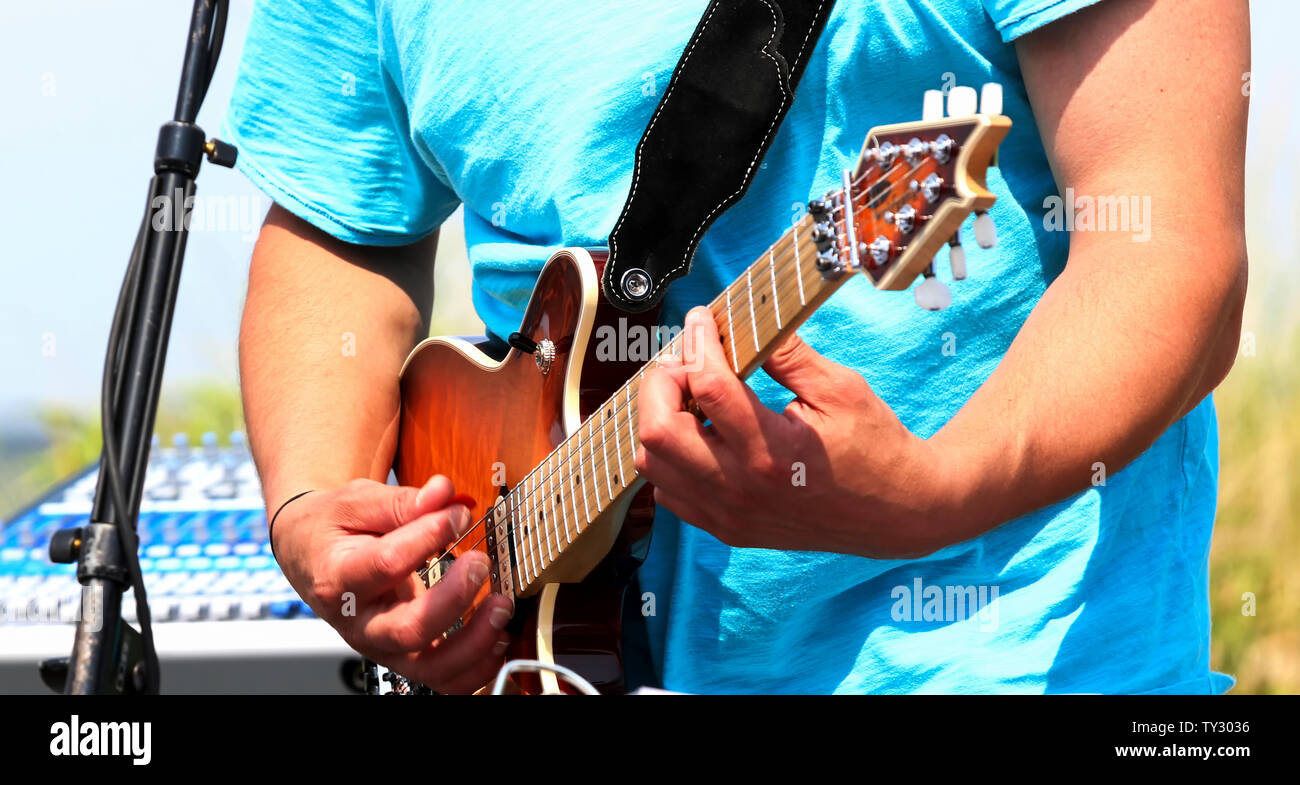 Close up of electric guitar being played outside at a beach by a man in a blue t-shirt. Stock Photo