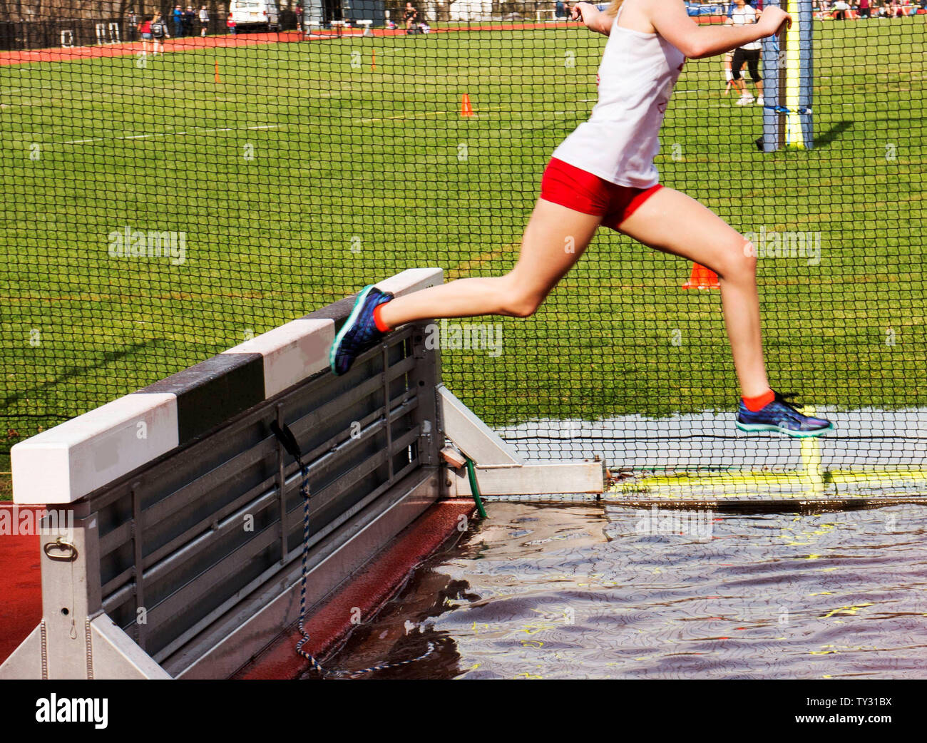A female runner going over the water jump in a steeplechase race Stock Photo