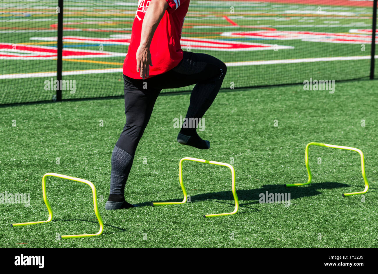 A high school track and field athlete is stepping over yellow mini hurdles with no shoes on to help develop foot strength. Stock Photo