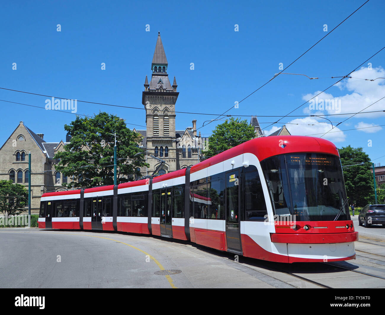 TORONTO - JUNE 2019:  A long articulated streetcar bends as it goes around a curve in front of a gothic style building at the University of Toronto on Stock Photo