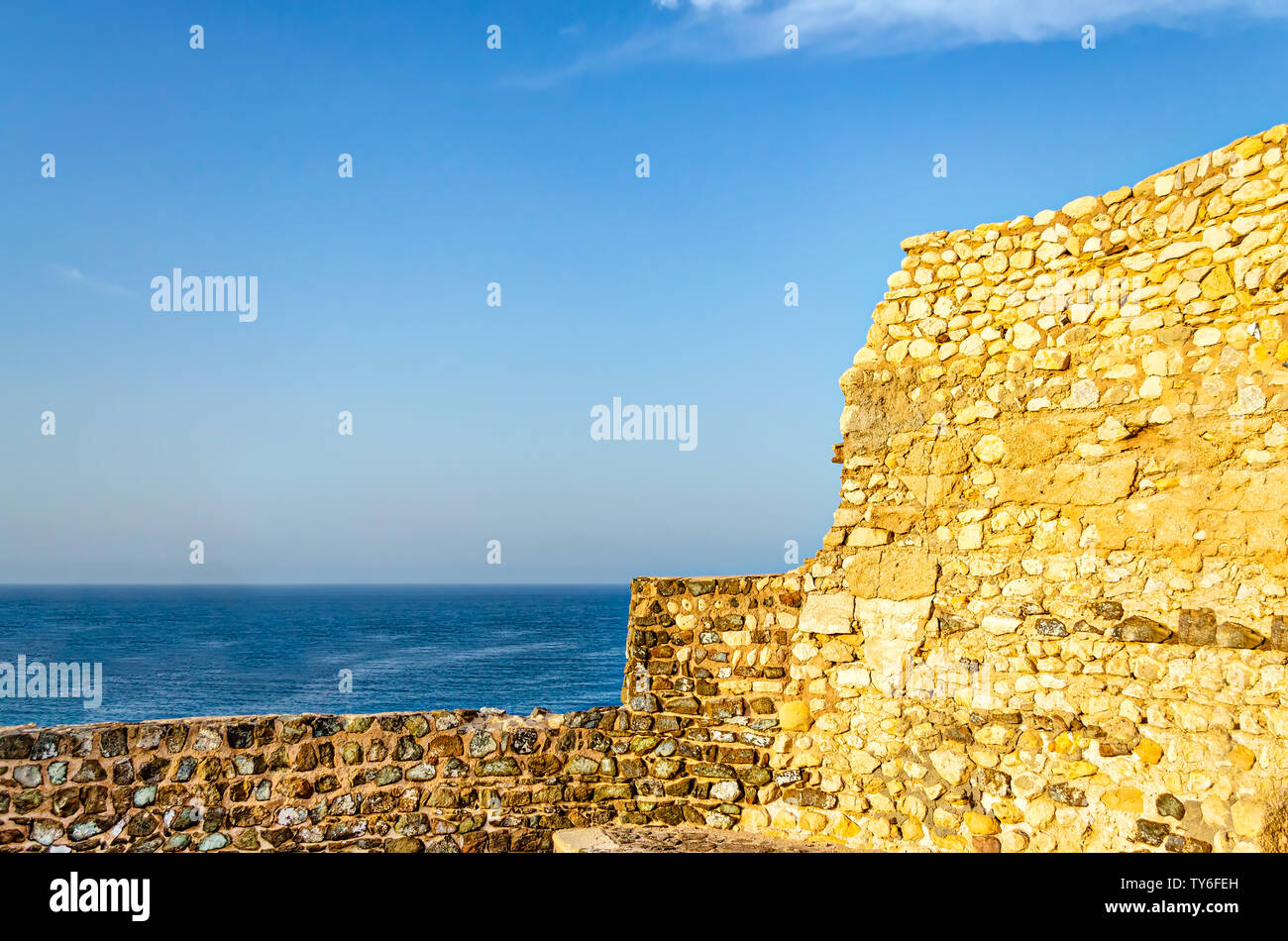 Old, abandoned and ruined fort wall opening to the blue sea with clear sky. From Muttrah, Muscat, Oman. Stock Photo