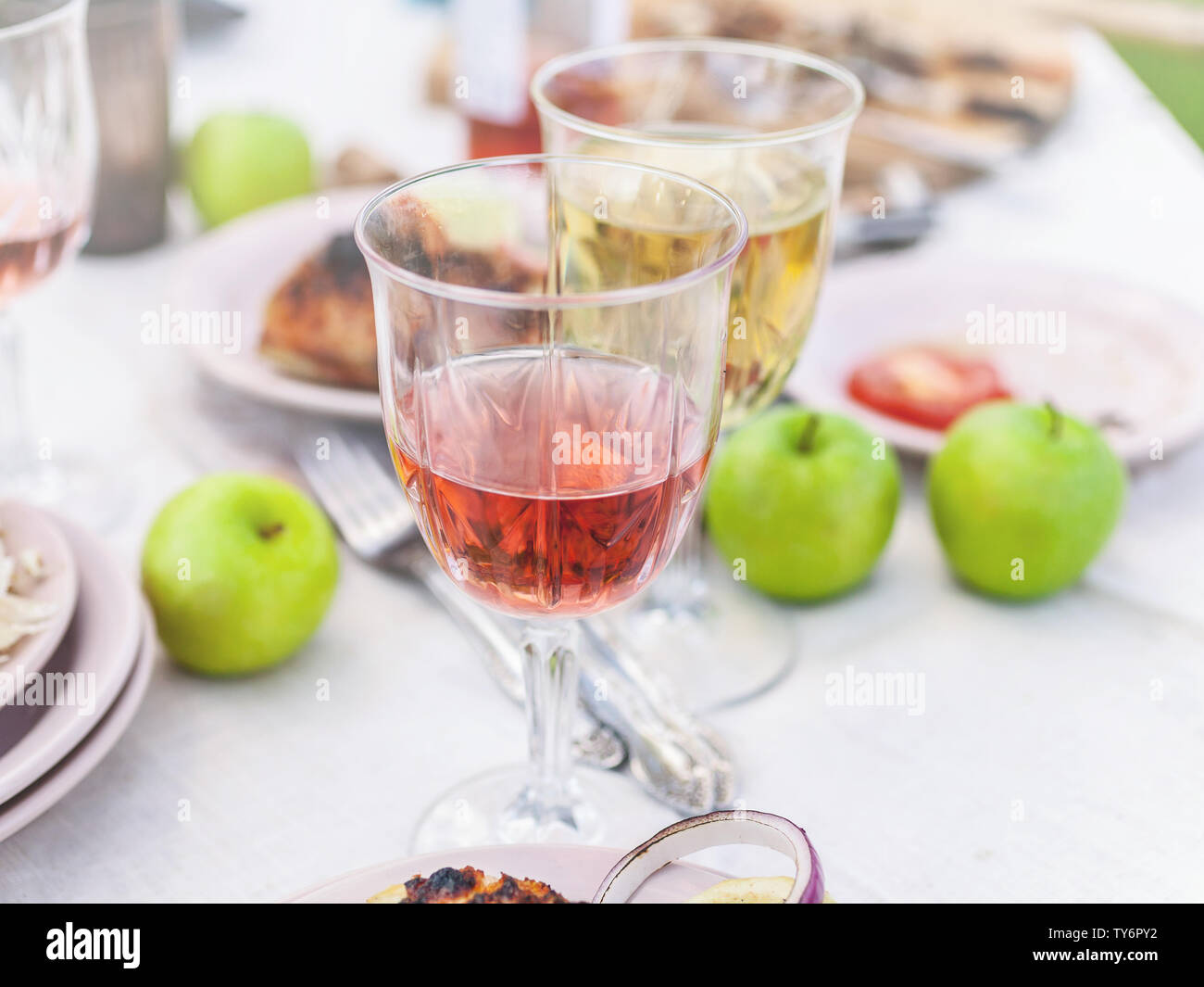 Grilled grouper, glasses with white and rose wine, plates, vegetables, salad and fruits on the table. Summer party in the backyard. Horizontal shot Stock Photo