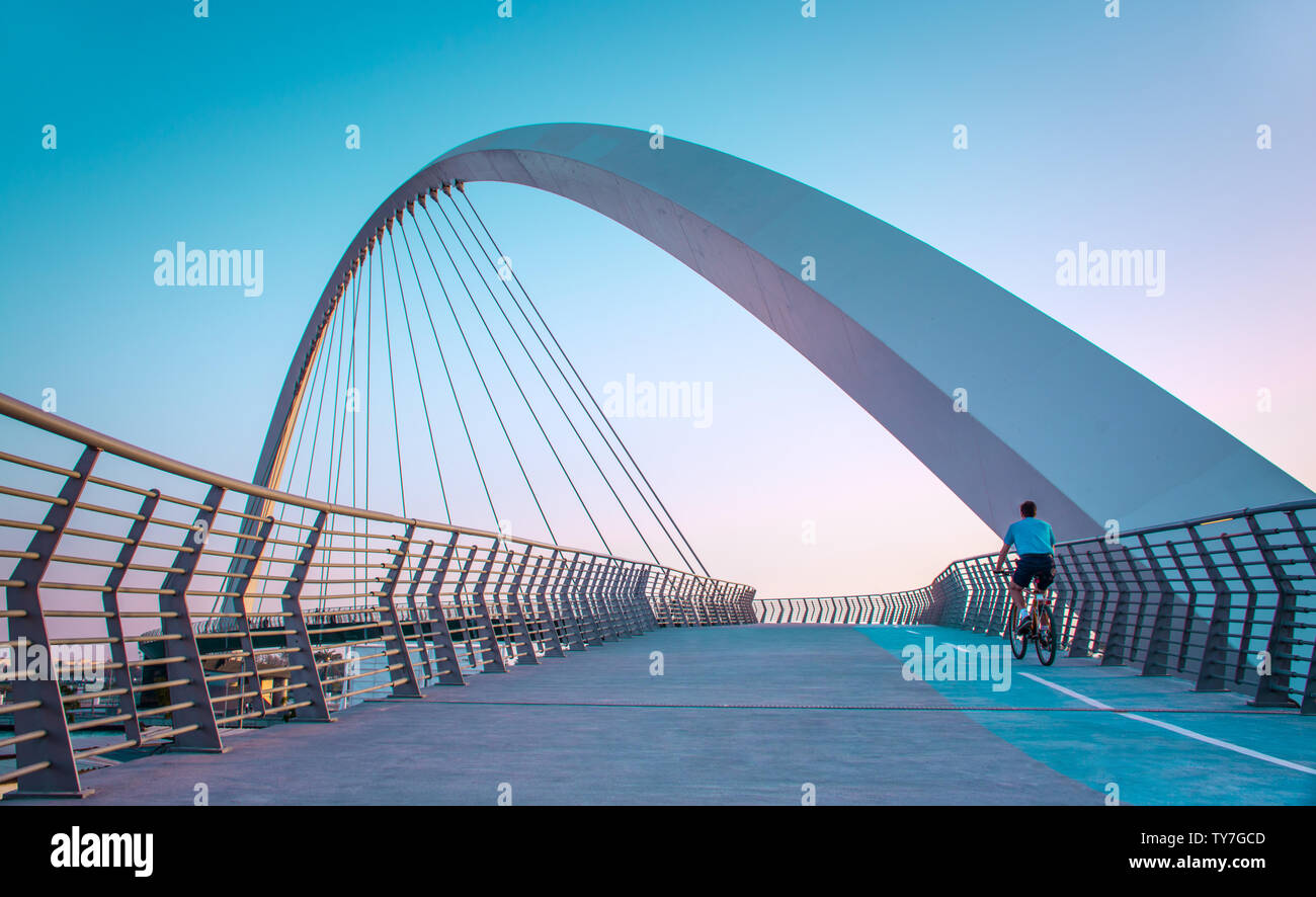 young man riding bicycle through Dubai water canal bridge famous attraction of Middle east modern architecture Bridge Stock Photo