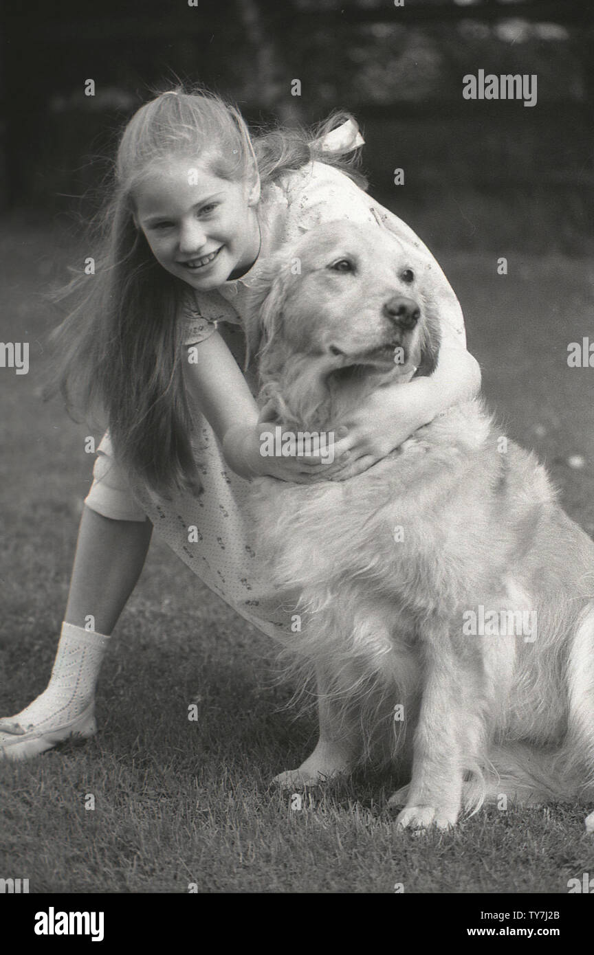 1980s, a young girl hugging her pet dog, a Golden Retriever. A medium to large-size hunting or gun dog  with a  friendly, gentle nature, they make good family pets and are well-suited to a suburban or country setting. Stock Photo