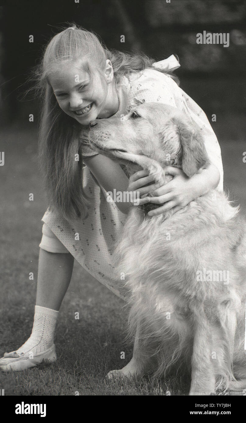 1980s, a young girl hugging her pet dog, a Golden Retriever. A medium to large-size hunting or gun dog  with a  friendly, gentle nature, they make good family pets and are well-suited to a suburban or country setting. Stock Photo