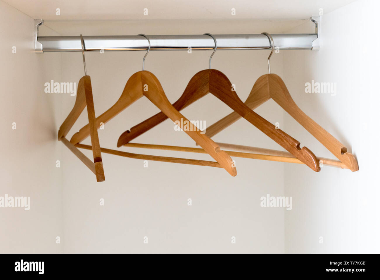 A horizontal detail view of an empty metal coatrack in a white wardrobe with four empty wooden coathangers Stock Photo