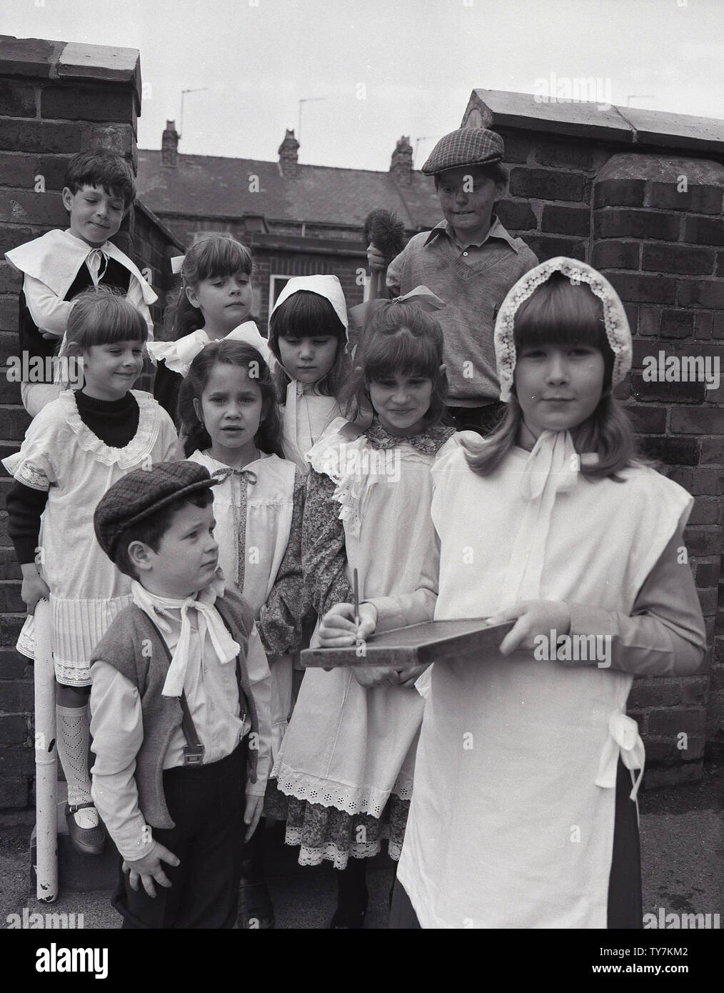 1980s, village school children outside dressed up in the clothes that there counterparts would have worn in Victorian times, Yorkshire, England, UK. The Victorian schoolgirl would wear a white cotton apron, often trimed with lace, worn over normal clothes as a means of protection. In addition, some girls would have worn a bonnet over their hair. Stock Photo