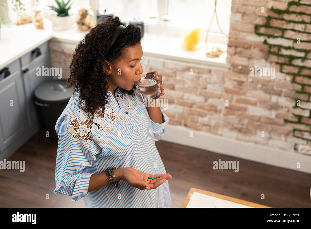 Pregnant lady taking her vitamins with water. Stock Photo