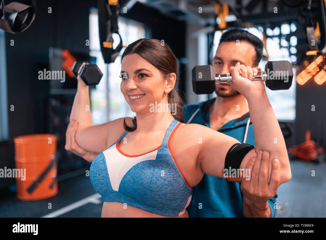 Trainer helping positive woman doing exercises for arms Stock Photo
