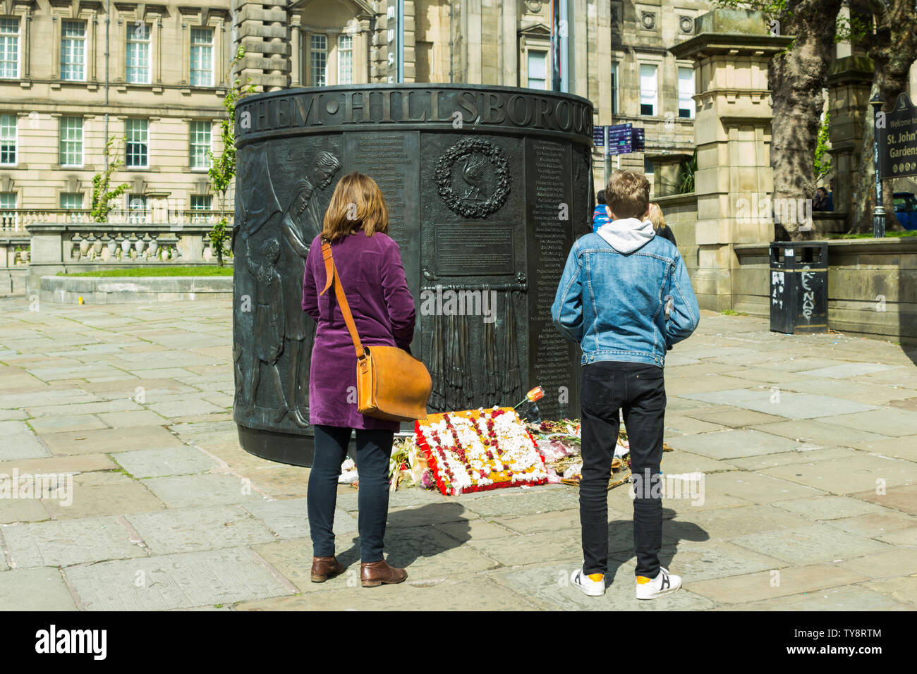 Two young people view the Hillsborough Disaster memorial on Old Haymarket, Liverpool, a 7ft high cylindrical bronze cast sculpture by Tom Murphy Stock Photo