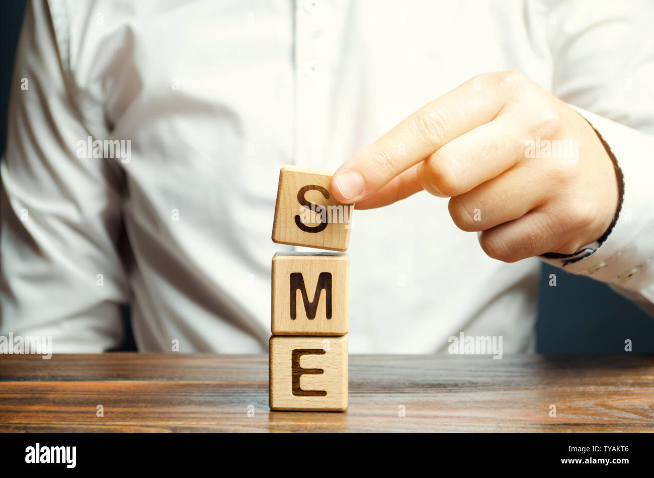 Businessman holds wooden blocks with the word SME. Small and medium-sized enterprises - commercial enterprises that do not exceed certain indicators. Stock Photo