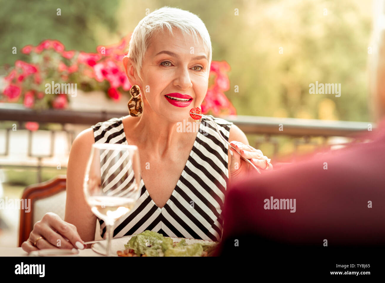 Mature woman with bright pink lips eating salad and talking to husband Stock Photo