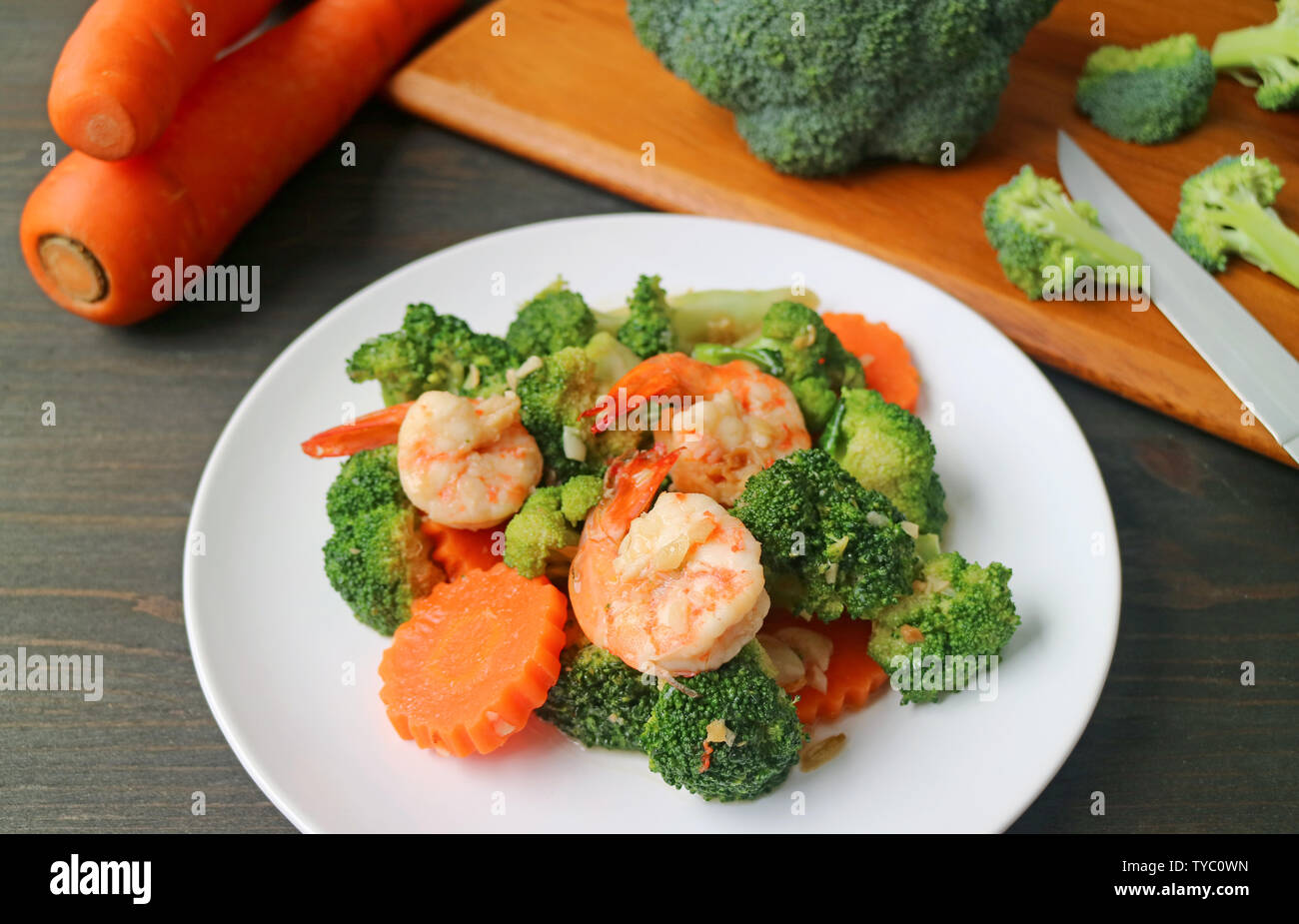 Plate of prawn stir fried with broccoli and carrot with blurry cut vegetables in background Stock Photo