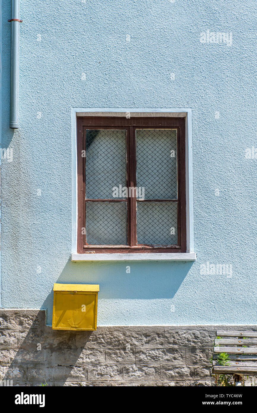 Window and a yellow postbox on a blue wall on a house, with shadows reminding flat design style Stock Photo