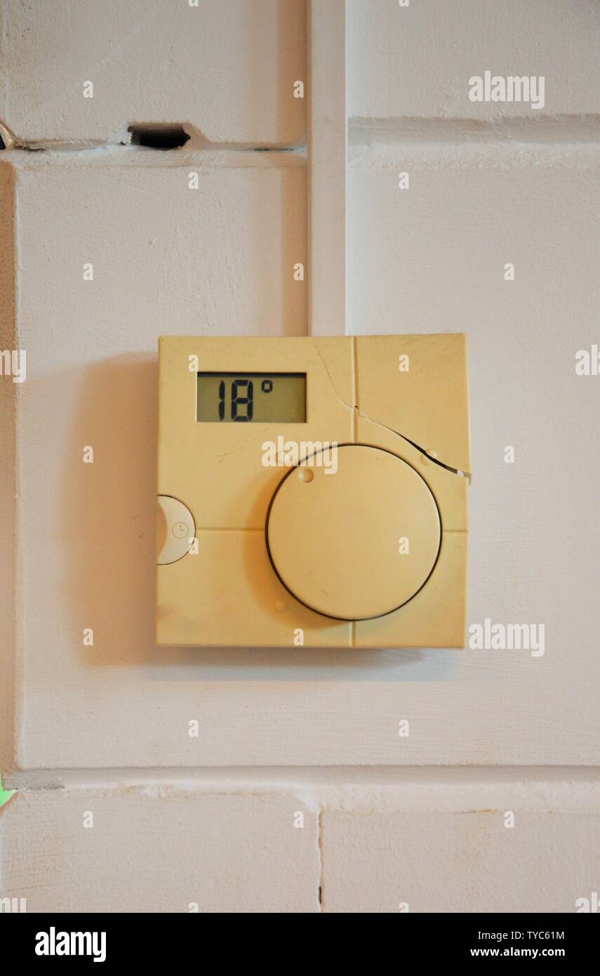 thermostat hanging on a white wall indicating a temperature of 18 degrees Celsius. Stock Photo