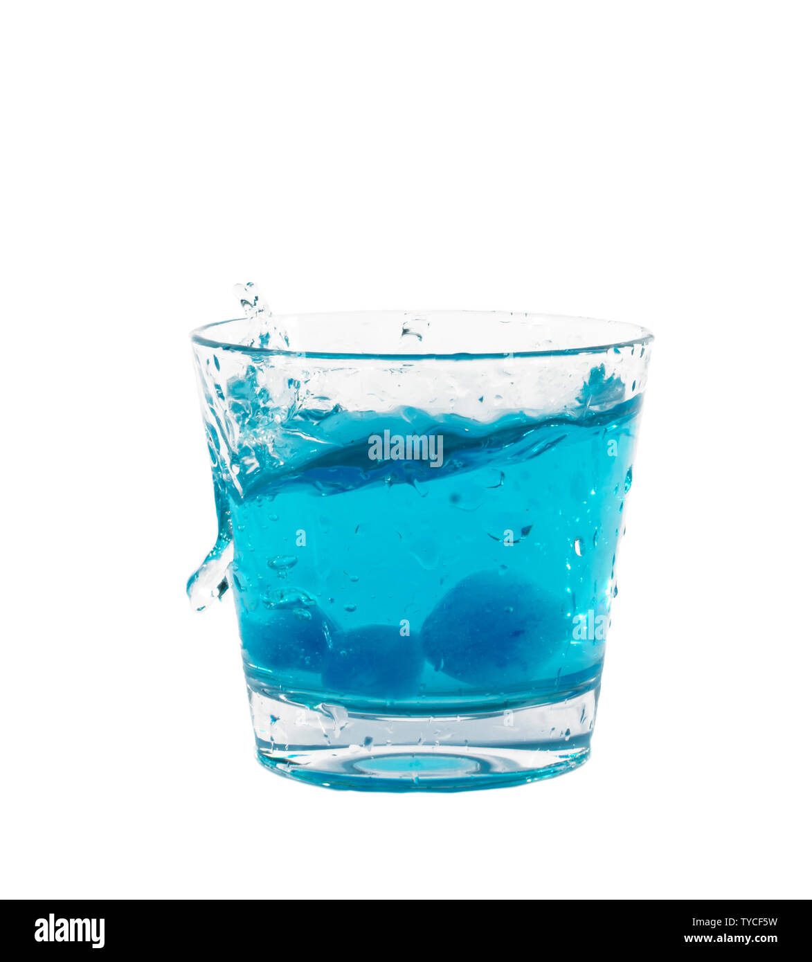 Blue ice cubes splashing into glass of water. Stock Photo