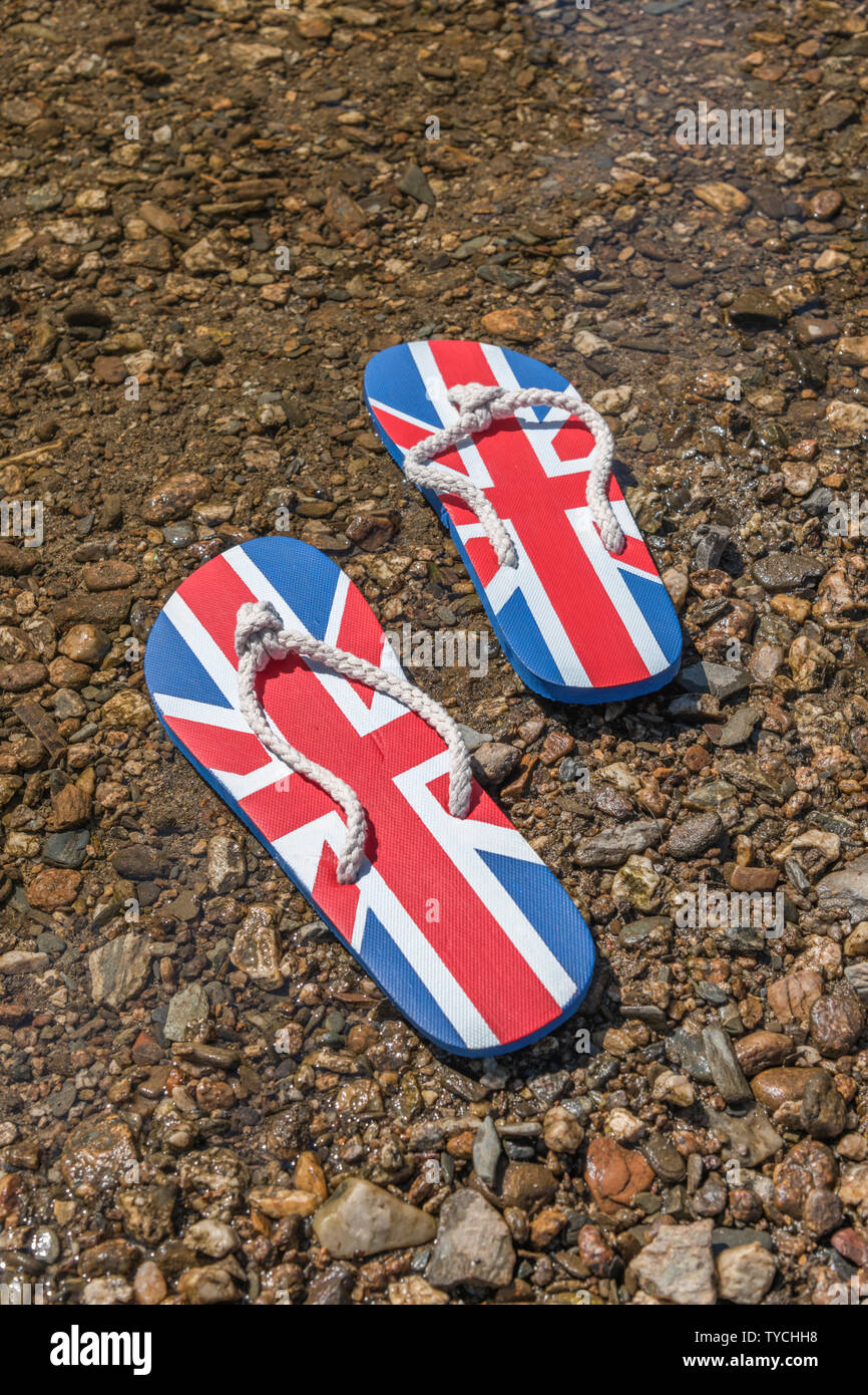 Union Jack flip-flops on river shingle. Metaphor 2021 UK staycation, holidays at home, staycation Cornwall, country break, flip flop footwear. Stock Photo