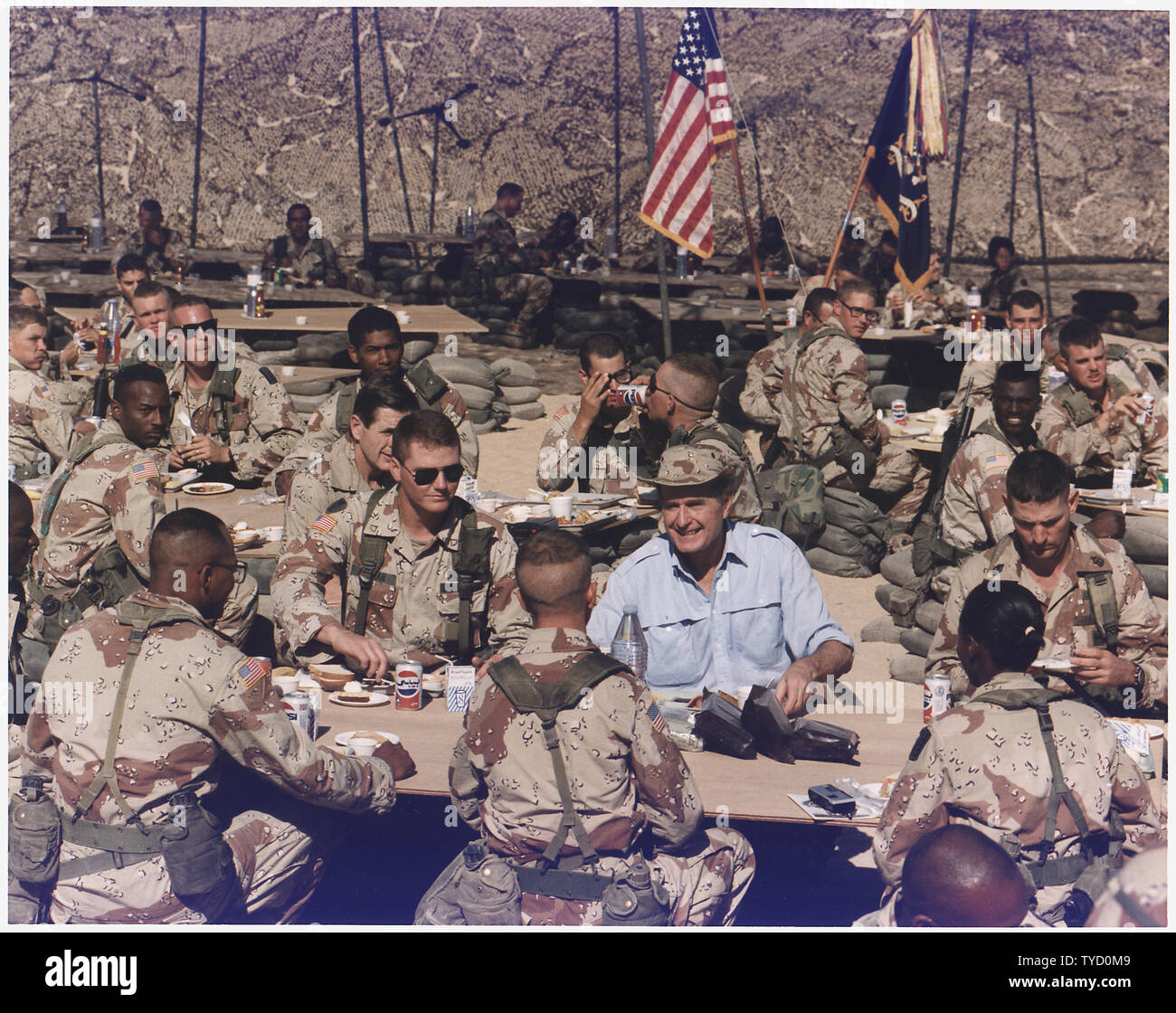Photograph of President George H. W. Bush Enjoying Thanksgiving Dinner with Troops; Scope and content:  This photograph documents President George H. W. and Barbara Bush visiting the U.S. Army 197th Infantry Brigade stationed in Saudi Arabia on November 22, 1990 during Operation Desert Shield.  President and Mrs. Bush had Thanksgiving dinner with the troops.  President Bush later shared a stage with Representative Bob Michel, Senator Robert Dole, Senator George Mitchell, and Representative Tom Foley and spoke to the soldiers. Stock Photo