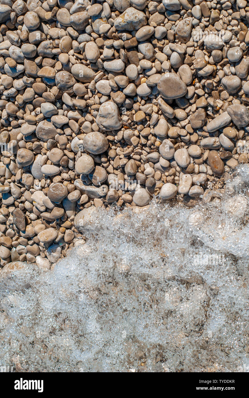 Smooth sea stones and sea waves foam, taken on a rocky beach Stock Photo