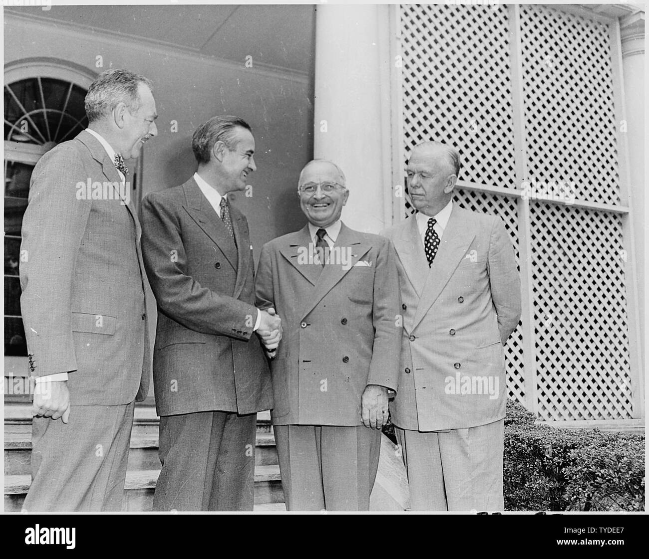 Photograph of President Truman in the White House Rose Garden shaking hands with W. Averell Harriman, Special Assistant to the President, prior to Harriman's leaving for Iran on a mission to resolve the British-Iranian oil dispute, as Secretary of State Dean Acheson (left) and Secretary of Defense George C. Marshall look on. Stock Photo