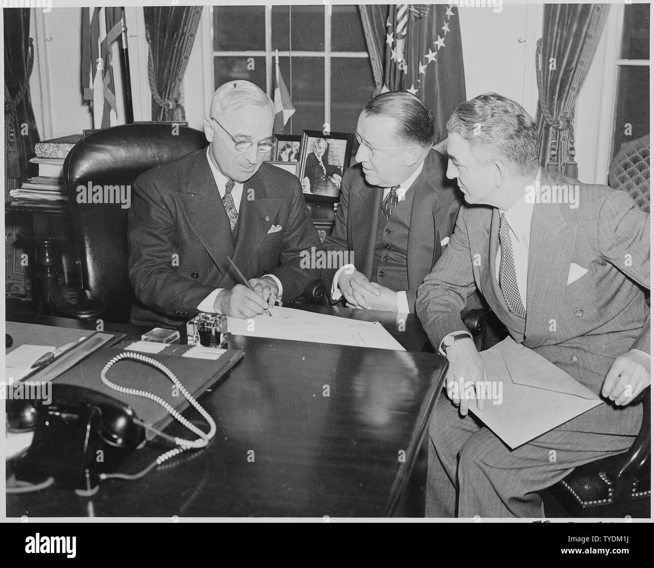 Photograph of President Truman signing S. 591, the Red Cross Reorganization Bill, at his desk in the Oval Office, as Chairman Basil O'Connor the American Red Cross and Howard Bonham look