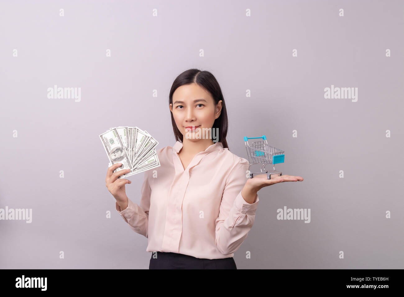 retail commercial business concept, Asian beautiful woman holding banknote money in hand and shopping cart in another hand isolated on grey background Stock Photo