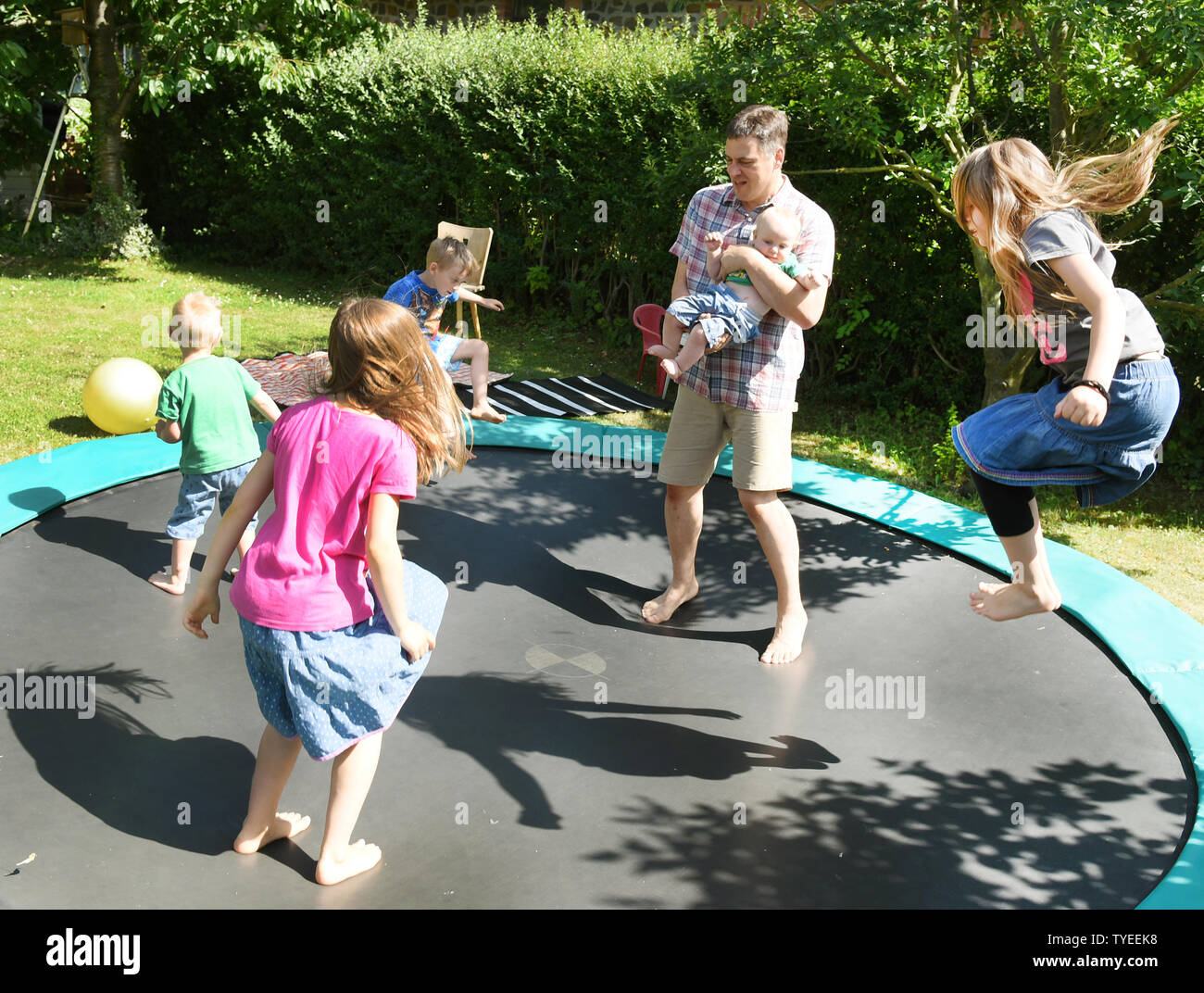 25 June 2019, Saxony, Schönwölkau: Father Stefan Fenchel jumps with five of his six children on the trampoline in the garden. Stefan Fenchel and his Canadian wife Emma moved from Bavaria to Leipzig in 2004 and now live in Schönwölkau with their six children, three girls and three boys between 12 and one year old. In the small village they have built an old house and enjoy the country life with their children. While at school in the neighboring city the German language is of course spoken, the whole family speaks English at home. (to dpa 'Where the children rich in Germany live - and how') Phot Stock Photo