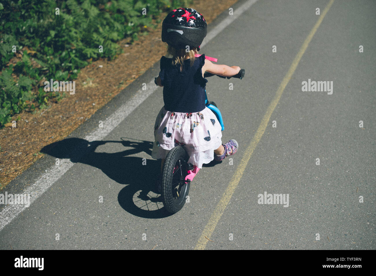 A young girl rides a run bike on a bike path beside a forest. Stock Photo