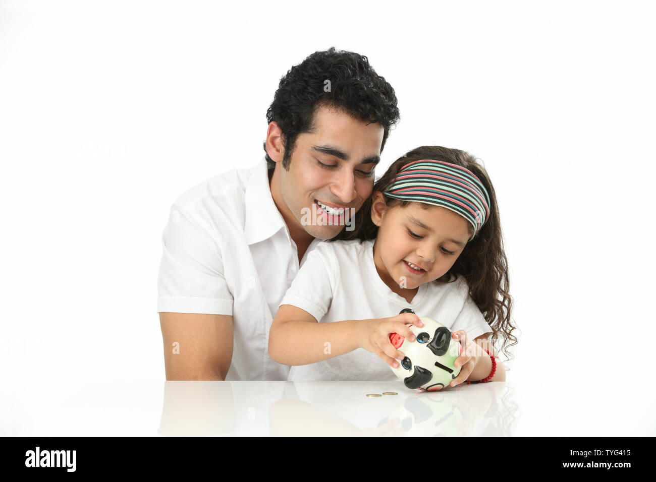 Indian girl putting coins into a piggy bank with her father Stock Photo ...