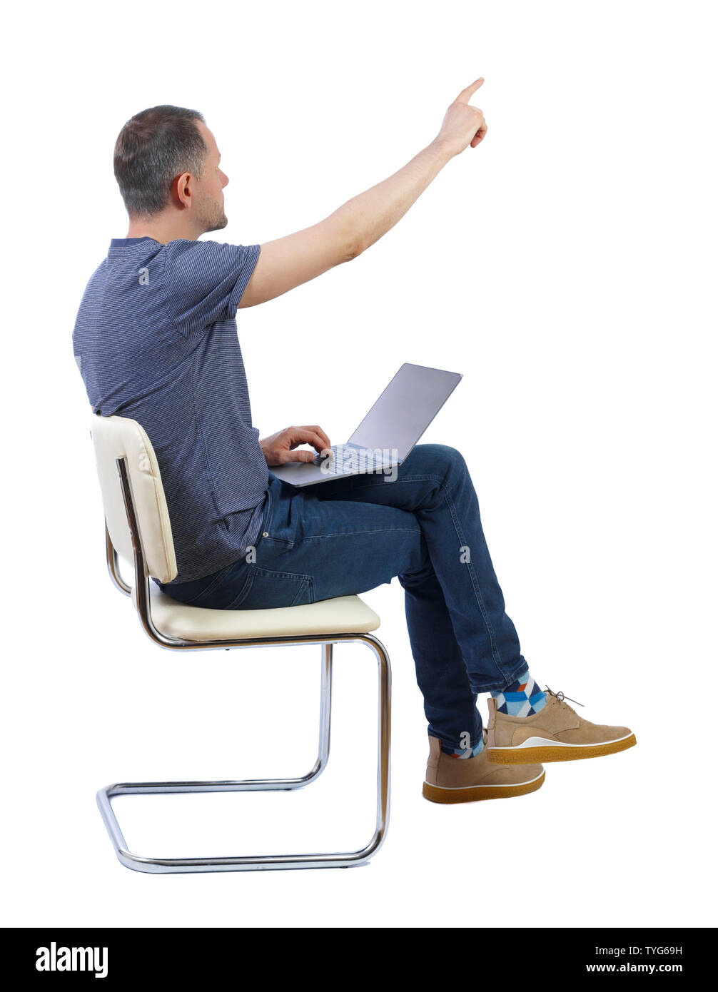 Side view of a man who sits on a chair with a laptop and points with his hand forward. A student at study raised his hand to clarify the issue. Rear v Stock Photo