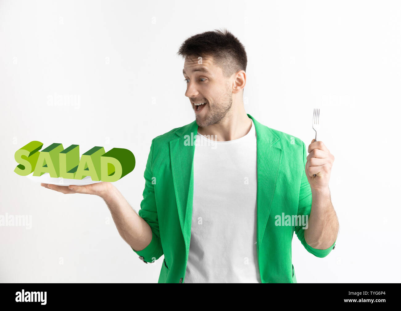 Man in green jacket with the folk isolated on white. Male model holding a plate with letters of word Salad. Choosing healthy eating, diet, organic nutrition and nature friendy lifestyle. Stock Photo